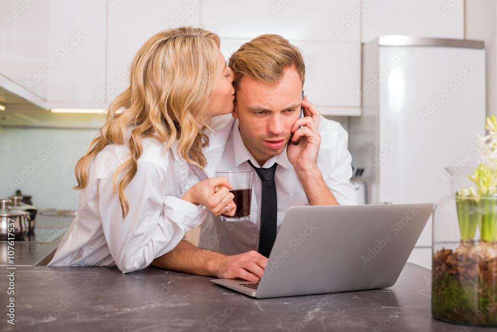 Woman kissing her husband on cheek while he is talking on the phone Woman kissing her husband on cheek while he is talking on the phone
