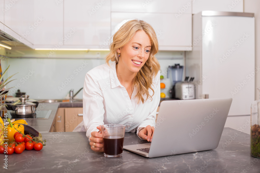 Woman working on computer while drinking coffee in kitchen Woman working on computer while drinking coffee in kitchen