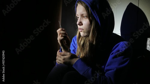 Addicted junkie teen girl with a syringe sitting on a floor and thinking about something. 4K UHD. photo