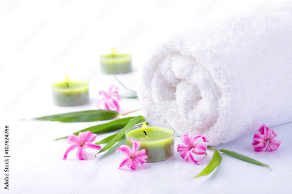 Spa Still Life - Weißes Handtuch mit Blüten und Kerzen vor weißem Hintergrund