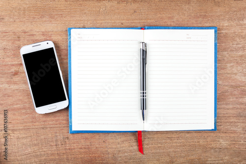 Blank open notebook with black pencil and mobile phone on wood t