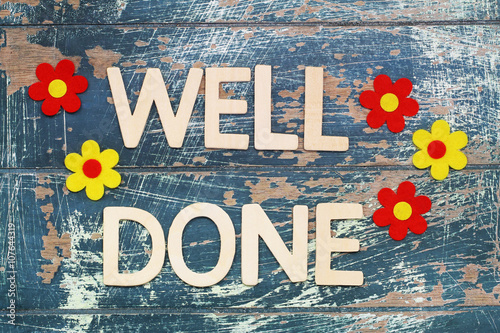 Well done written with wooden letters on rustic surface and colorful flowers
