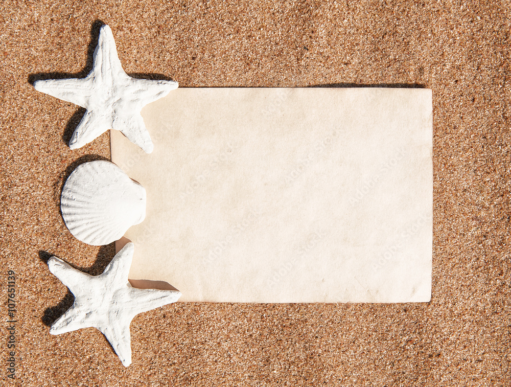 Summer background with paper andseashells on the sand Summer background with paper andseashells on the sand