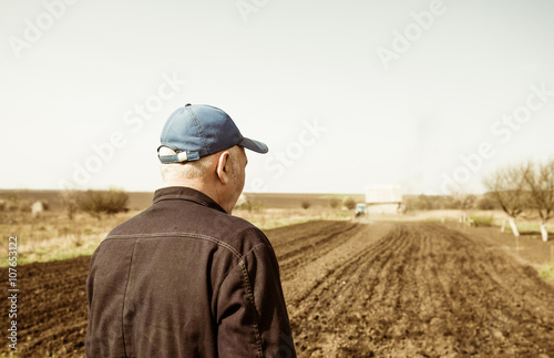 senior farmer looking at tractor plowing soil