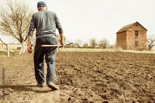 farmer with rake walking on plowed spring ground