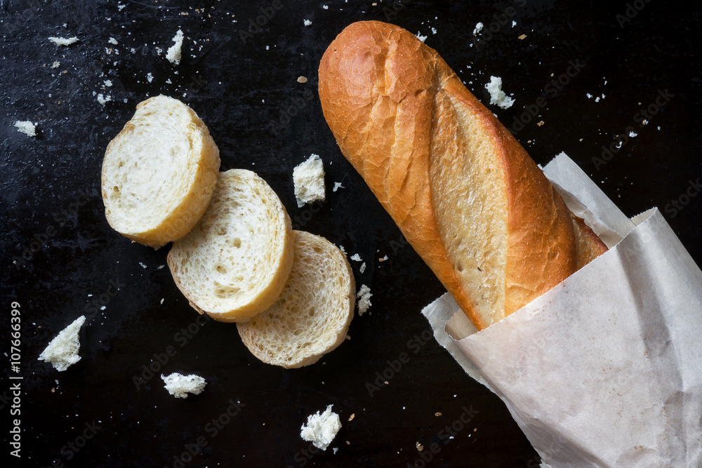 Sliced french baguette with crumbs on dark background