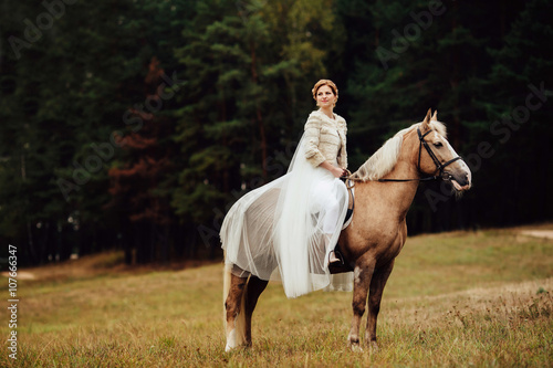 gorgeous young bride sitting on brown horse in forest © SPY_studio