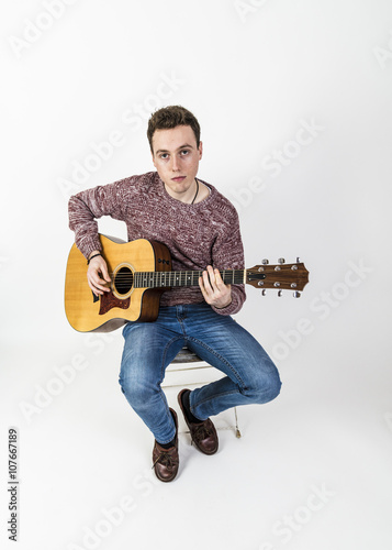 teenage guitar player sits on a chair and plays western guitar
