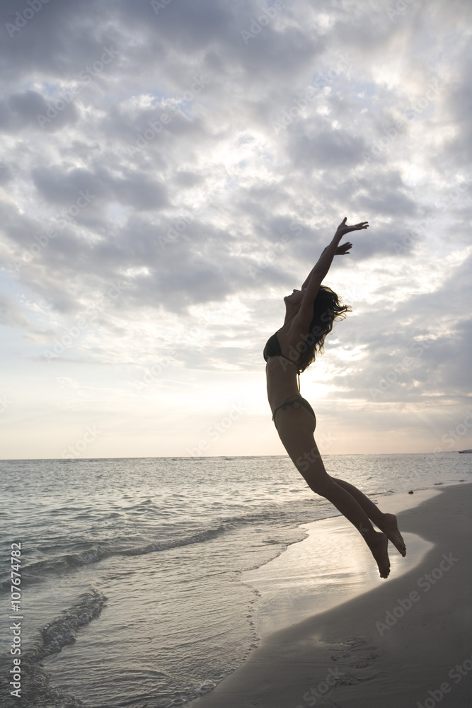 femme au coucher du soleil à la mer sautant en l'air