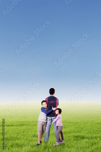 Two kids hugging their father at field