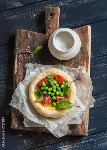 Puff pastry egg tartlet with fresh green peas and cherry tomatoes on wooden rustic board. Delicious breakfast or snack