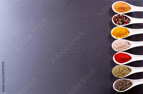 various spices in ceramic spoons on dark background