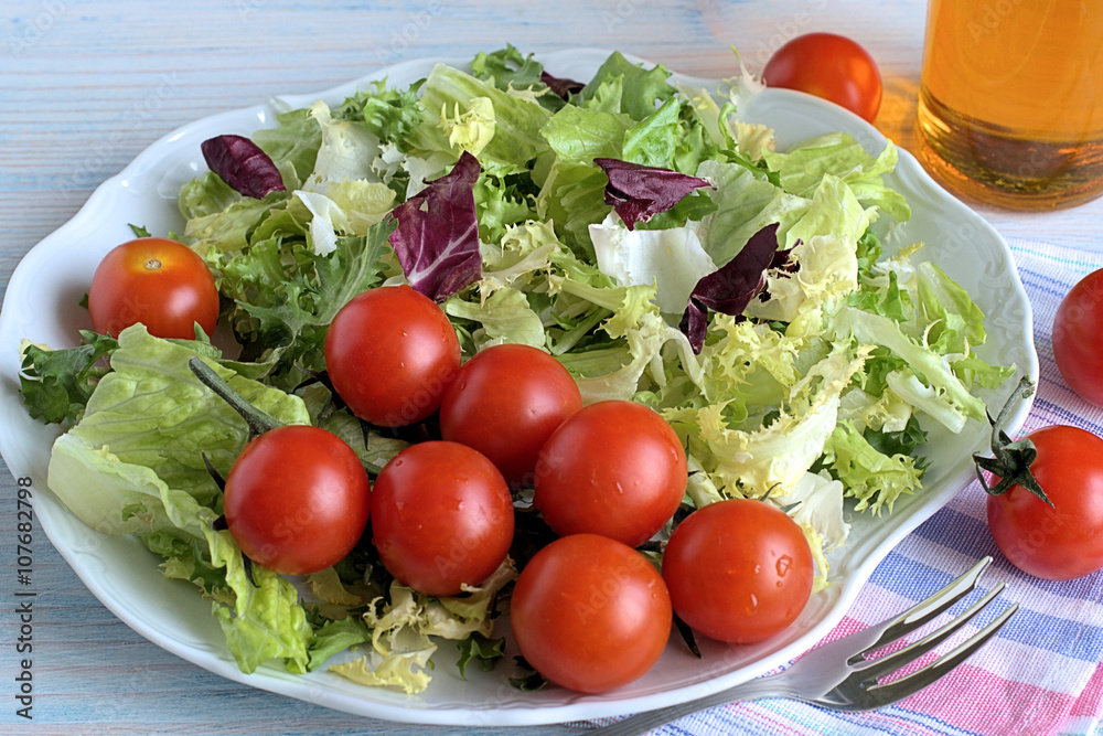 Fresh lettuce and cherry tomatoes . Leaves of fresh lettuce and cherry tomatoes on a white dish on a blue wooden background. Fresh lettuce and cherry tomatoes . Leaves of fresh lettuce and cherry tomatoes on a white dish on a blue wooden background.