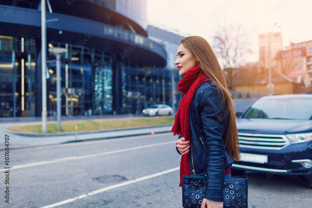 Fashion shot of pretty young woman over city background, wearing red scarf. City lifestyle. Female fashion