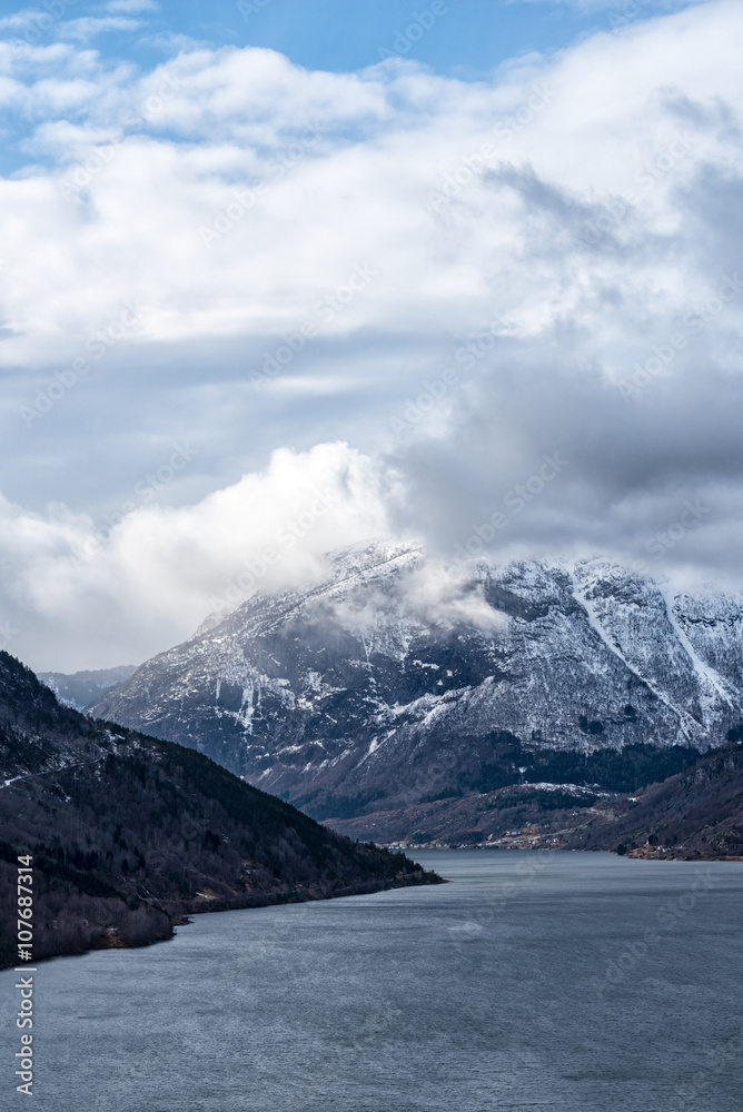 Mountain in fjord landscape with low hanging clouds. Vertical composition