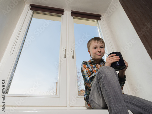 Young boy with cup sitting on window.