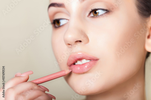 Sensual picture of woman face with makeup pencil on lips. Applying lips contour