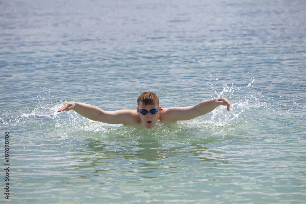 young sporting man swims in the sea butterfly stroke style.