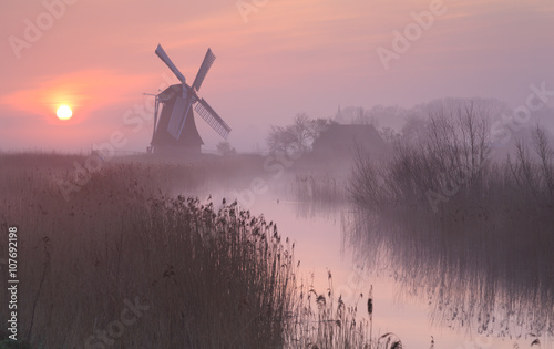 Foggy, pink sunrise in Holland with a traditional windmill in the wetlands.
