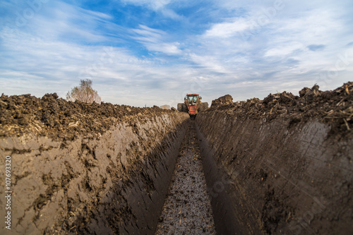 Tractor with double wheeled ditcher digging drainage canal photo