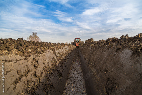 Tractor with double wheeled ditcher digging drainage canal