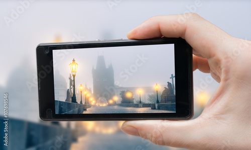 Tourist is photographing Charles Bridge in Prague with smartphone.