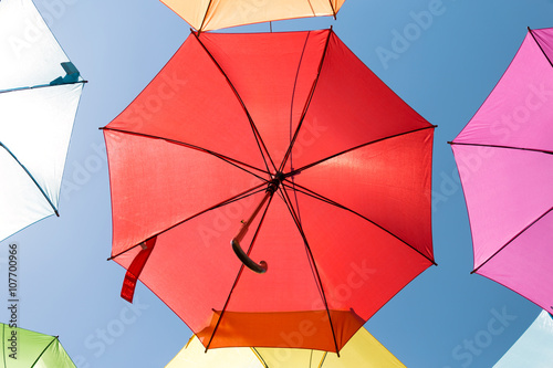 One red umbrella on blue sky surrounded by other colorful umbrellas