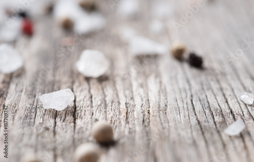 Closeup of whole peppercorns and crystal sea salt on rustic wood as background