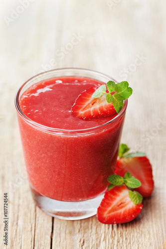 Strawberry smoothie in a glass decorated with mint leaves on rustic background, fresh fruit juice is red, detox food, diet and healthy breakfast