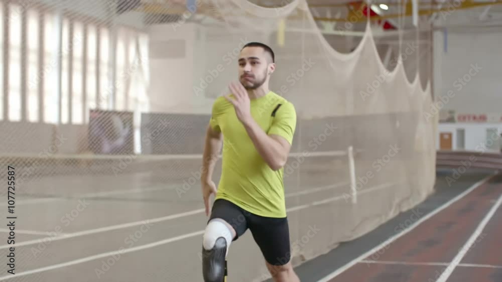 Paralympic athlete with prosthetic leg running on track in practice, slow motion 