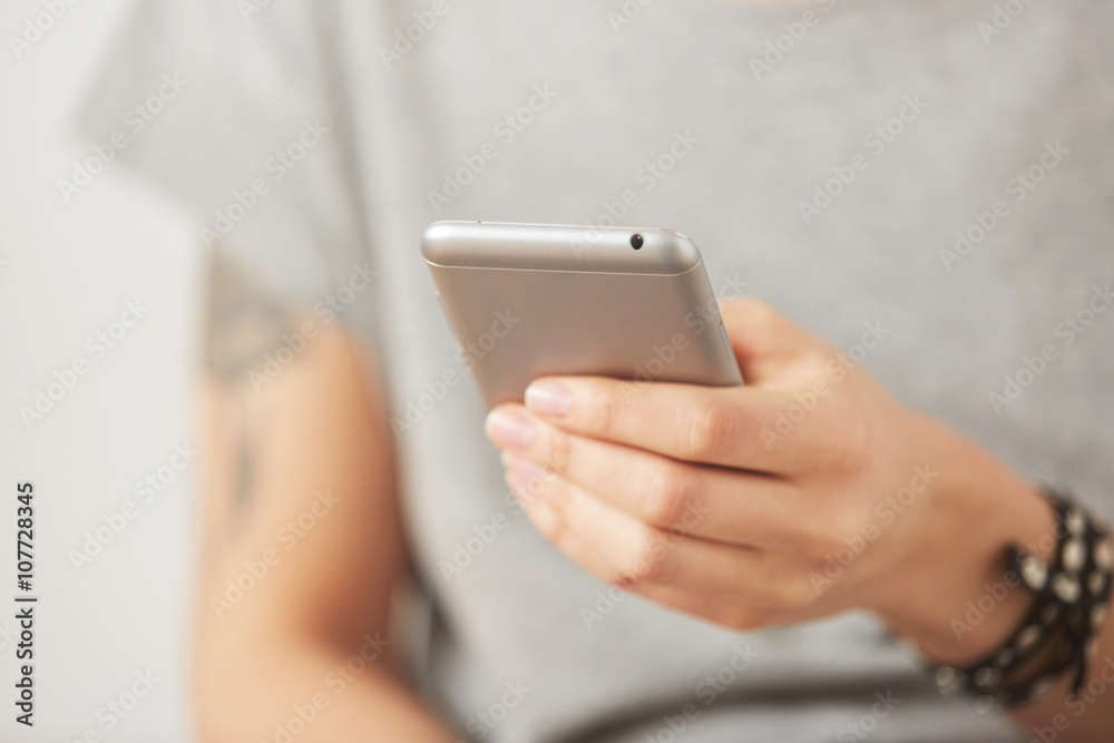 Cropped shot view of female hands holding cell phone, young woman texting on mobile telephone during work break on the gray background