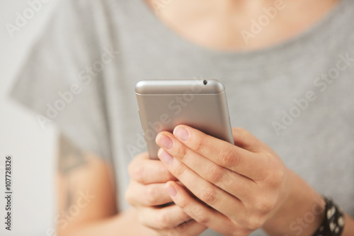 Cropped shot view of female hands holding cell phone, young woman texting on mobile telephone during work break on the gray background