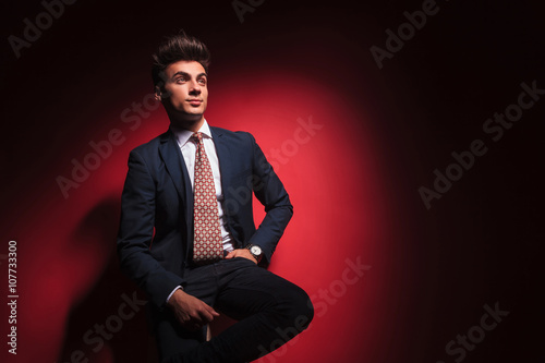 businessman in black with red tie posing seated in studio