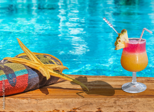 serviette, étoile de mer et cocktail sur planche au bord de piscine bleue 