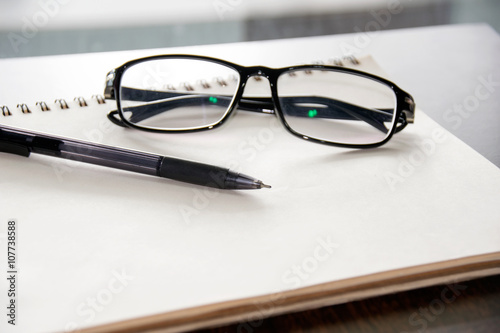 Close up Glasses and pen on notebook on table