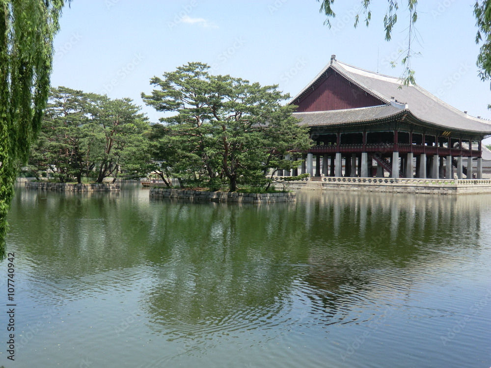 A Lake And Palace In Seoul, South Korea
A lake with stone walled islands and trees. A large wooden Palace building. A weeping willow tree, set against a clear blue sky. A Lake And Palace In Seoul, South Korea
A lake with stone walled islands and trees. A large wooden Palace building. A weeping willow tree, set against a clear blue sky.