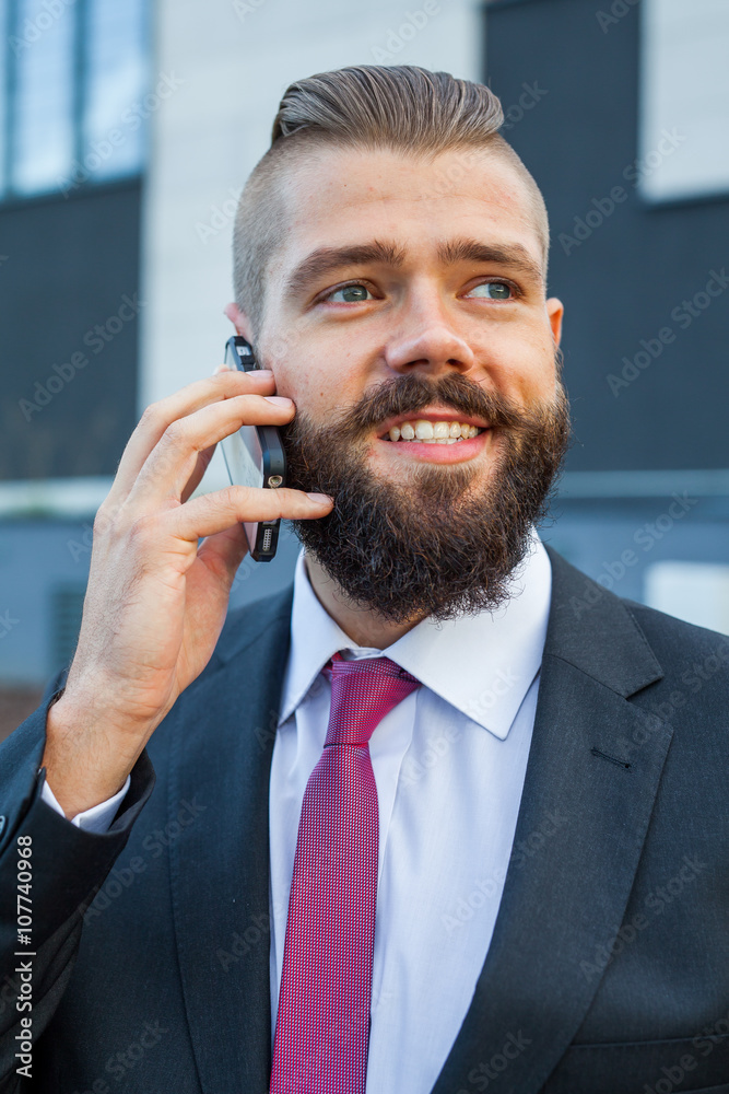 Young bearded businessman wearing eyeglasses using mobile phone