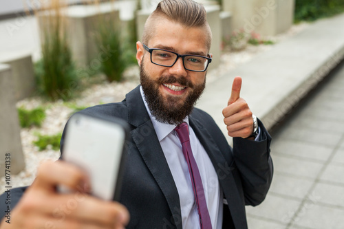 Young happy bearded businessman standing outside office building