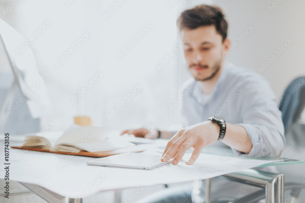 Young man in a modern office design sketching construction project design in a note book computer and drinks coffee Young man in a modern office design sketching construction project design in a note book computer and drinks coffee