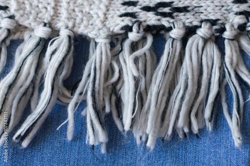 Knitted piece of cloth with woolen fringe and jeans, selective focus