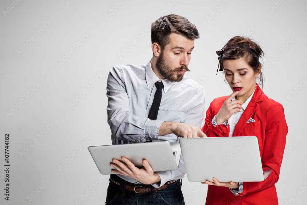 The young businessman and businesswoman with laptops  communicating on gray background