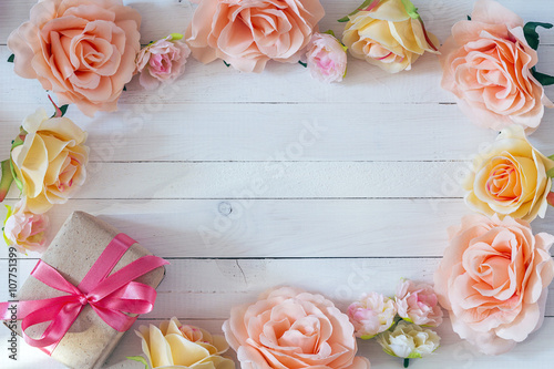 Frame of rose flowers on white painted wooden background with gi