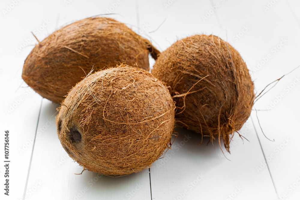 Three whole not split coconuts, on a wooden white plank background. Some coconuts in the group. Three whole not split coconuts, on a wooden white plank background. Some coconuts in the group.