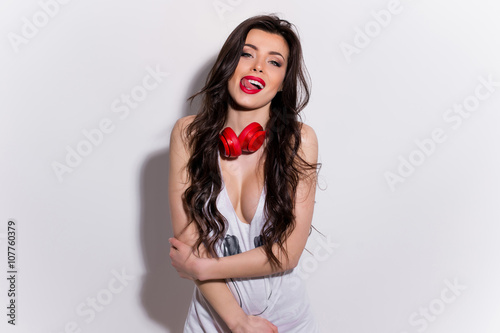 Young, happy and sexy girl with red lips with headphones in a t-shirt showing tongue and licking teeth