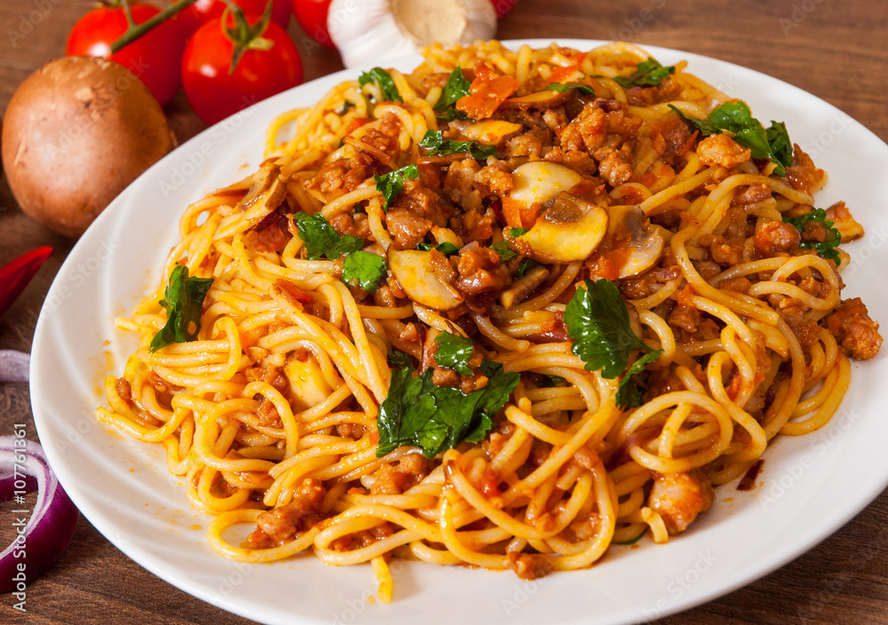 spaghetti with mushroom, vegetables and minced meat in a plate on wooden table