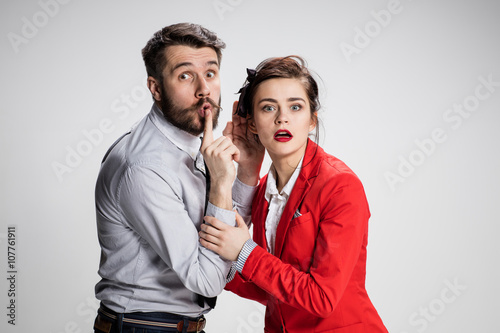 Young man telling gossips to his woman colleague at the office