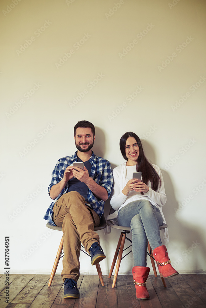 Smiling man and woman are sitting on chairs with smartphones Smiling man and woman are sitting on chairs with smartphones