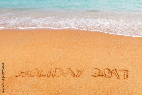 Inscription "Holiday 2017" made on the beach by the blue sea