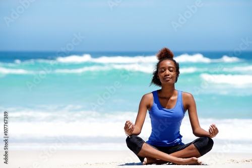 Young african woman meditating in yoga pose at the beach