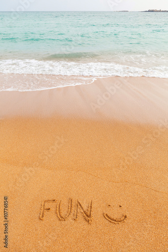 Inscription "FUN :)" made on the beach by the blue sea